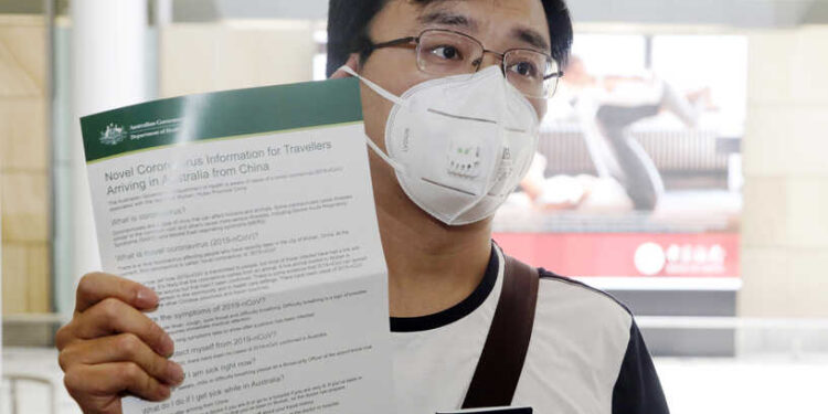 Passenger Kevin Ouyan shows an information pamphlet he was given on arrival at Sydney airport in Sydney Thursday, Jan. 23, 2020, on a flight from Wuhan, China. China closed off a city of more than 11 million people as part of a radical effort to prevent the spread of a deadly virus that has sickened more than 500 people and has begun to spread to other cities and countries in the region. (AP Photo/Rick Rycroft)