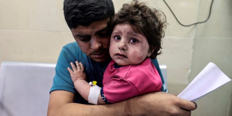 A Palestinian man holds an injured girl awaiting medical care at al-Shifa hospital, after an Israeli air strike in Gaza city, on May 11, 2021. (Photo by MAHMUD HAMS / AFP)